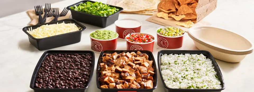 Chipotle Build Your Own catering spread with black trays of chicken, rice, beans, guacamole, salsa, cheese, and tortillas