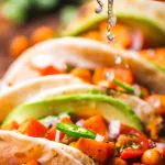Colorful tacos topped with fresh vegetables, avocado, and lime drizzle on a wooden board