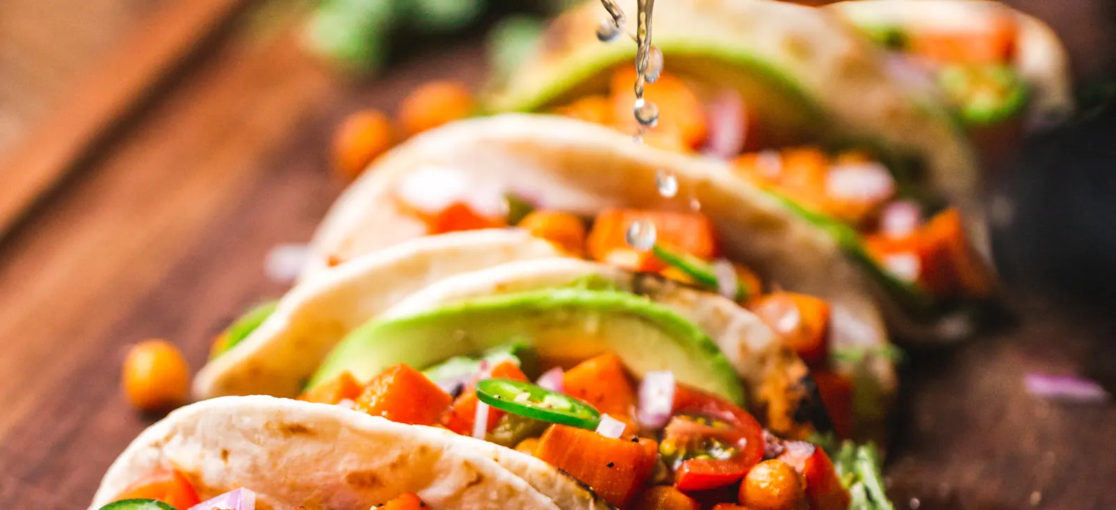 Colorful tacos topped with fresh vegetables, avocado, and lime drizzle on a wooden board