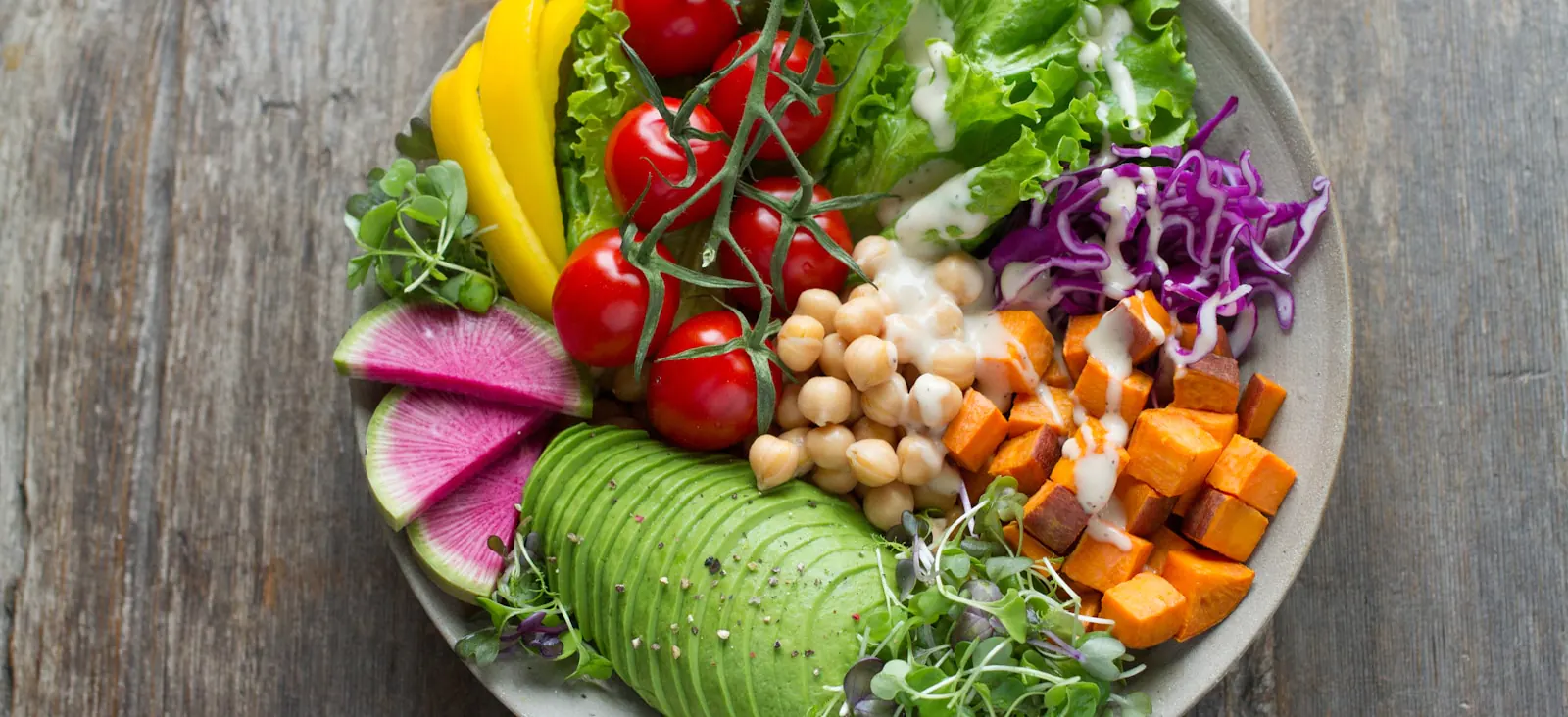 Colorful vegan buddha bowl with chickpeas, avocado, sweet potato, tomatoes, cabbage, and greens