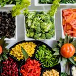 Colorful vegetable catering spread with broccoli, peppers, corn, olives, and fresh produce in white serving containers