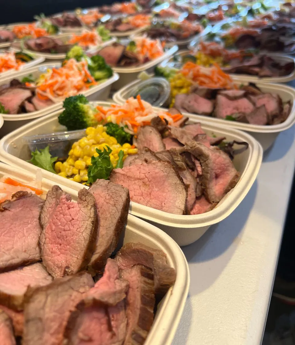 Rows of individually packaged sliced steak boxed lunches with sides and slaw arranged for anchor day delivery