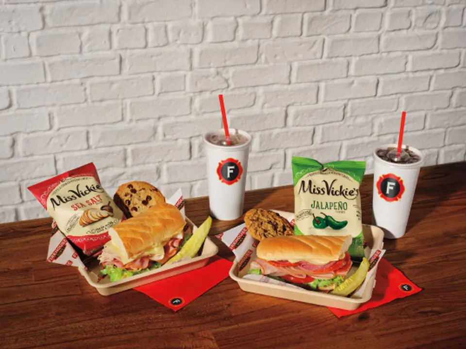 Two individually packed boxed lunches with subs, kettle chips, cookies, and bottled drinks for office distribution