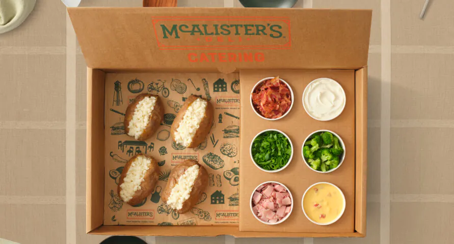 McAlister's Deli Spud Bar catering box with four giant baked potatoes split open and six toppings ramekins (bacon, sour cream, green onion, broccoli, ham, queso)