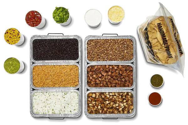QDOBA Chicken and Steak Hot Bar catering setup with foil pans of grilled chicken, steak, fajita veggies, cilantro lime rice, black beans and pinto beans, plus ramekins of salsa, pico de gallo, sour cream, cheese, guacamole and a fresh QDOBA-branded tortilla chip bag