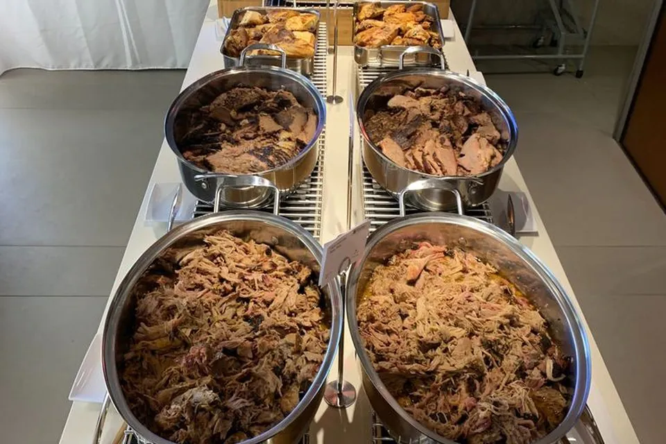 Atlanta office BBQ buffet line with oval chafing dishes of pulled pork, sliced brisket, fried chicken, sides, and bread rolls