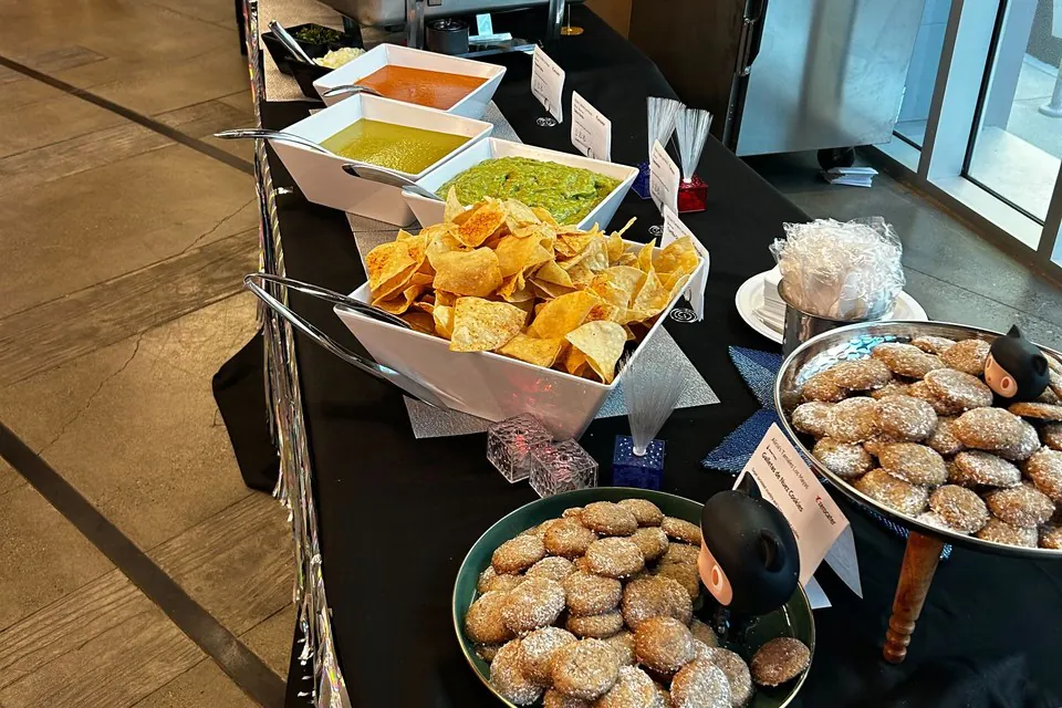 Tex-Mex office buffet line with tortilla chips, guacamole, salsas, chafing dishes, and sopapilla-style fried dessert pastries on a black tablecloth in Austin