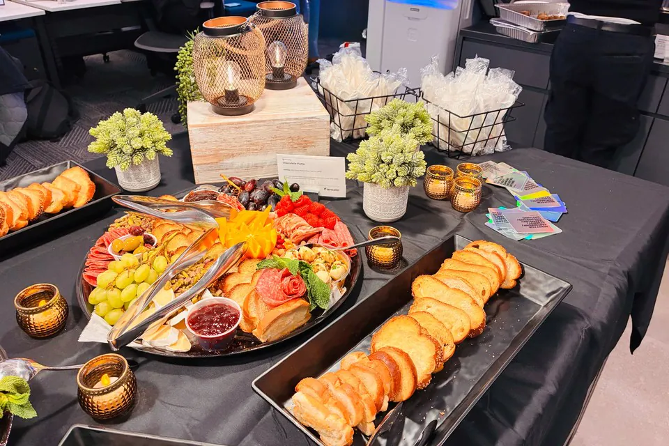 Charcuterie board reception with cured meats, grapes, jam, and sliced baguette on a black-draped office table for a full-service corporate event in Austin