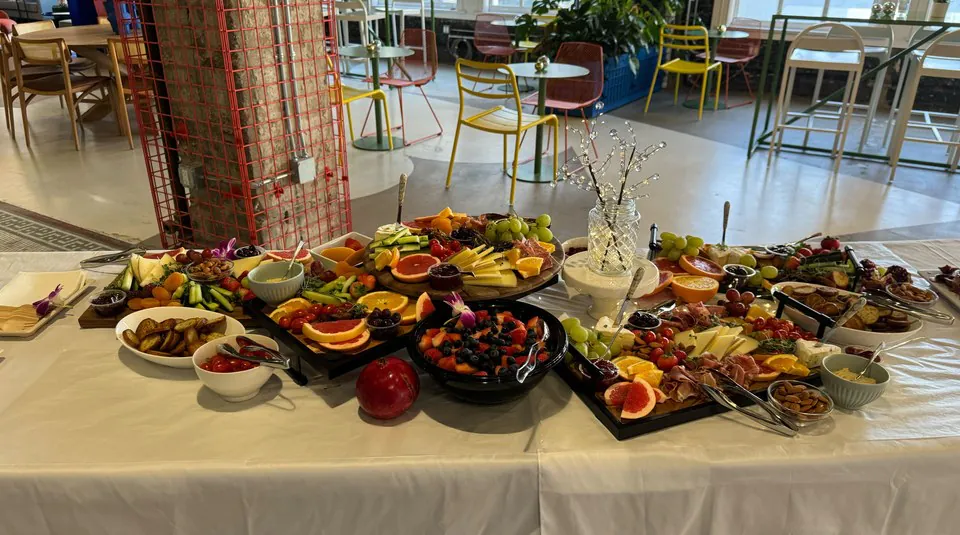 Real Zerocater family-style grazing spread on a long office table: charcuterie, fruit platters, cheese boards, marinated vegetables, dips, and shared bowls running the length of the table with office seating visible in the background