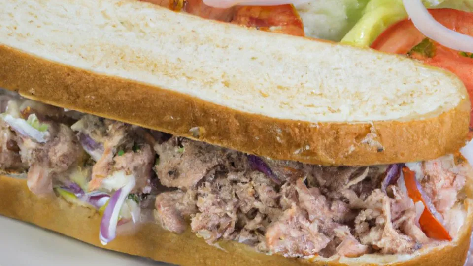 Close-up of a Capriotti's-style sub with hand-pulled pulled meat, fresh lettuce, ripe tomato, and red onion on white sub bread