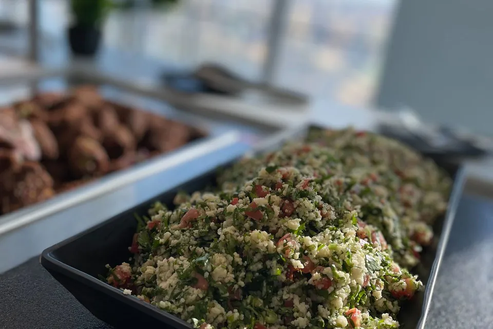 Mediterranean office buffet with a tabbouleh platter and kofta kebabs in front of floor-to-ceiling windows overlooking a downtown D.C. high-rise skyline