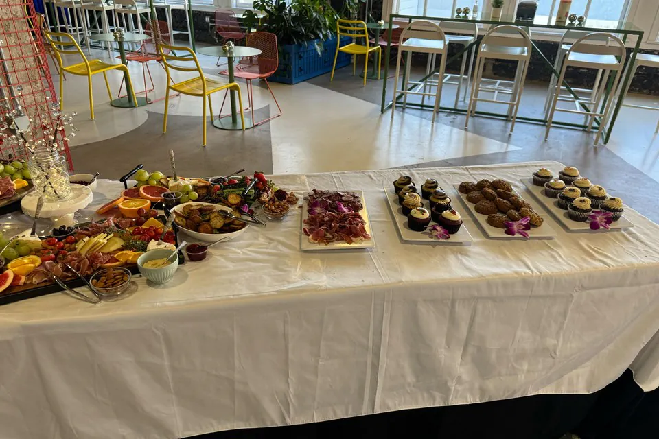 Full-service corporate reception spread with a charcuterie and fruit board, cured-meat platter, and assorted dessert platters on white linen in a D.C. event space