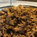 Close-up of slow-smoked chopped beef brisket piled high in a stainless catering pan, ready for an office BBQ buffet