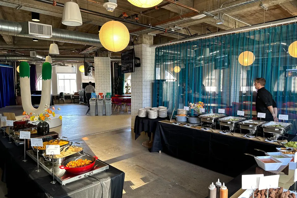 Large office buffet line with chafing dishes and chef attendant during active service in a modern loft venue with paper lantern lighting