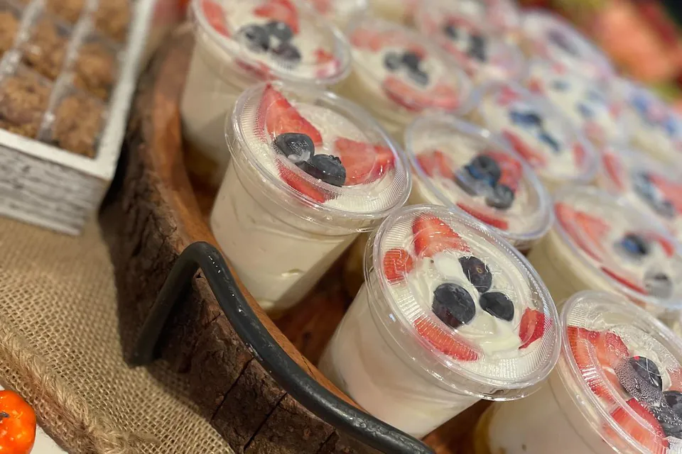 Individual yogurt parfait cups with strawberries and blueberries on a wooden serving board, individually packaged for a corporate breakfast event