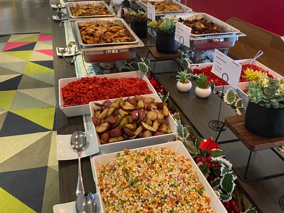 Colorful office holiday buffet with couscous salad, roasted potatoes, chicken and Mediterranean sides on a long catering table