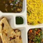 Indian corporate catering boxed thali tray with chana masala, saffron basmati rice, mixed vegetable curry, naan flatbread, and green chutney