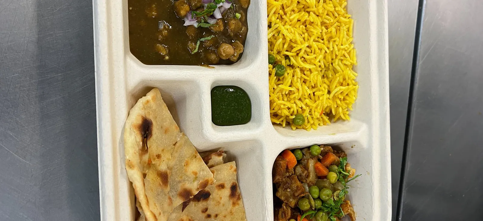 Indian corporate catering boxed thali tray with chana masala, saffron basmati rice, mixed vegetable curry, naan flatbread, and green chutney