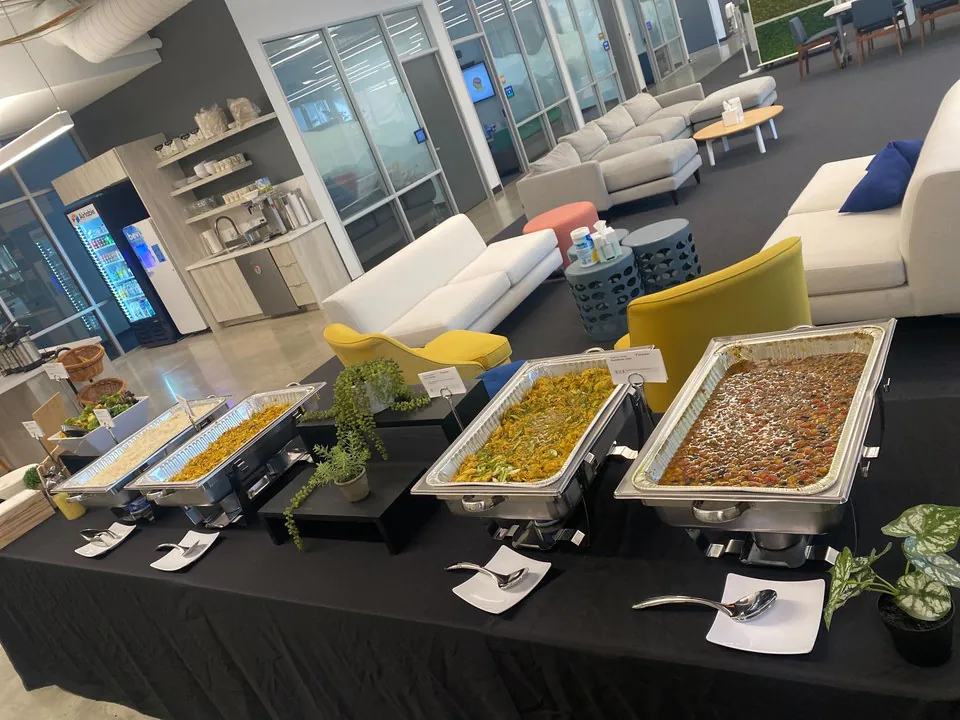 Real Zerocater Mexican catering buffet with four chafing trays of cilantro-lime rice, stewed peppers and onions, picadillo, and ranchero-style braised meats on black linen in a modern office lounge