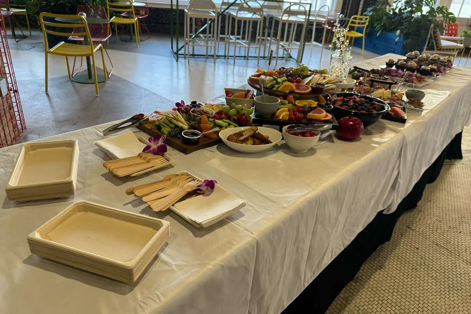 Long grazing table with charcuterie, fresh fruit, cheese, salads, and pastries laid out on white linen in an office cafe
