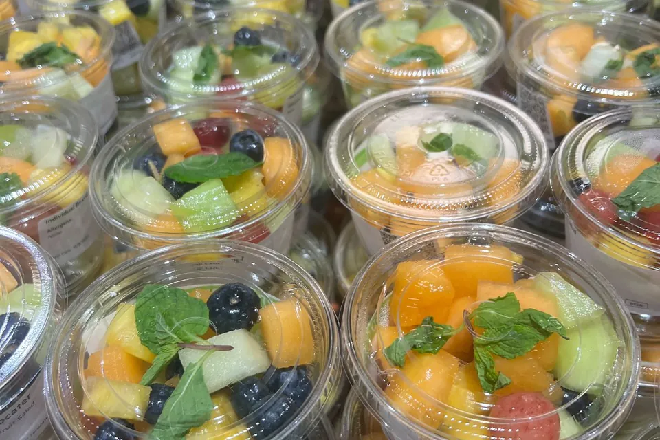 Clustered clear plastic catering cups filled with fresh melon, grapes, blueberries, and raspberries topped with mint sprigs, the visual analog to Playa Bowls' individual bowl format