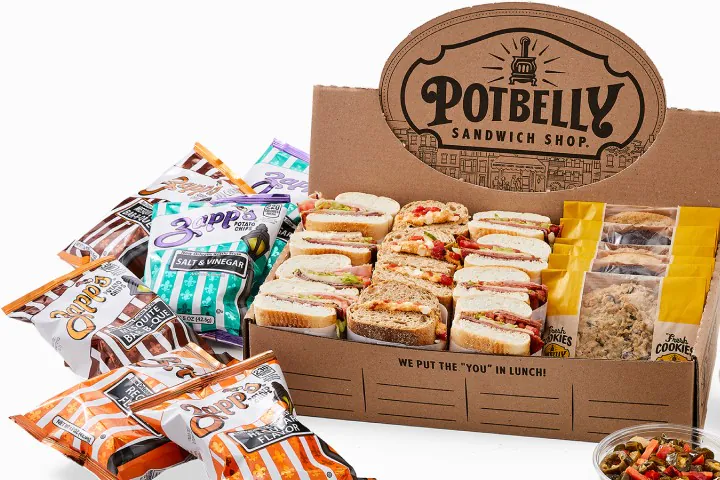 Branded Potbelly Bundle box stuffed with wrapped toasted sandwich halves, single-serve chips bags, and Potbelly oatmeal chocolate-chip cookies for office catering