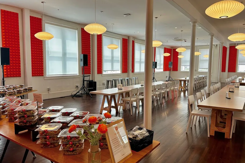 Tech office dining hall with rows of boxed lunches and stacks of clear meal containers lined up across a long wooden table for a large company meal