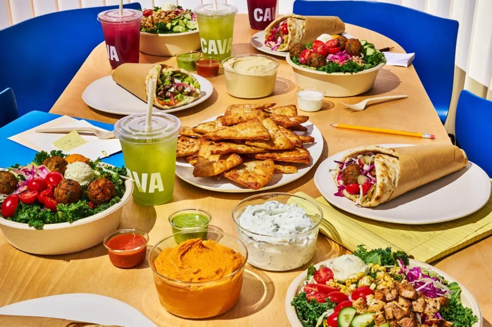 A CAVA catering table with Mediterranean bowls, pita wraps, hummus and tzatziki dips, pita chips and house-made juices