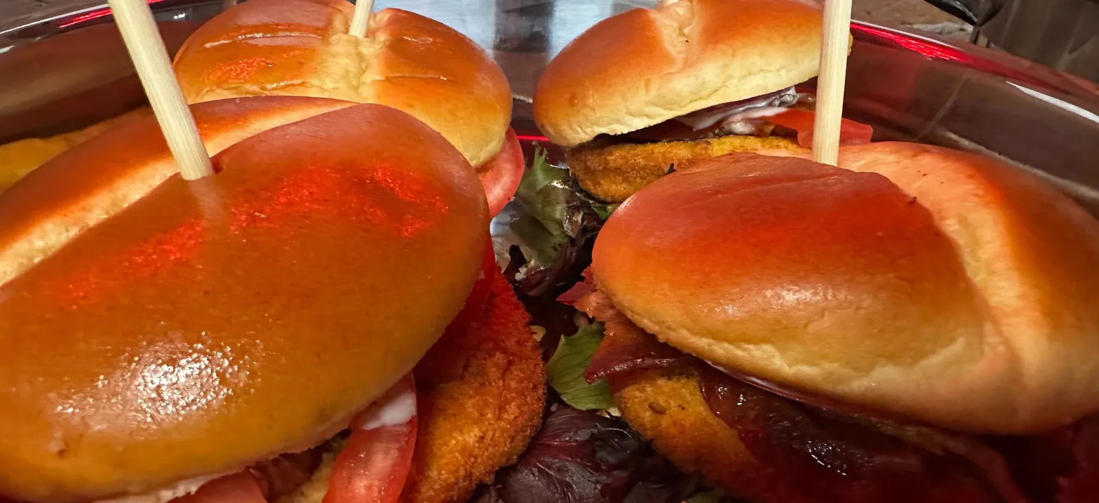 Catering chafer of crispy fried chicken sandwiches on golden brioche buns with lettuce and tomato, held with serving picks