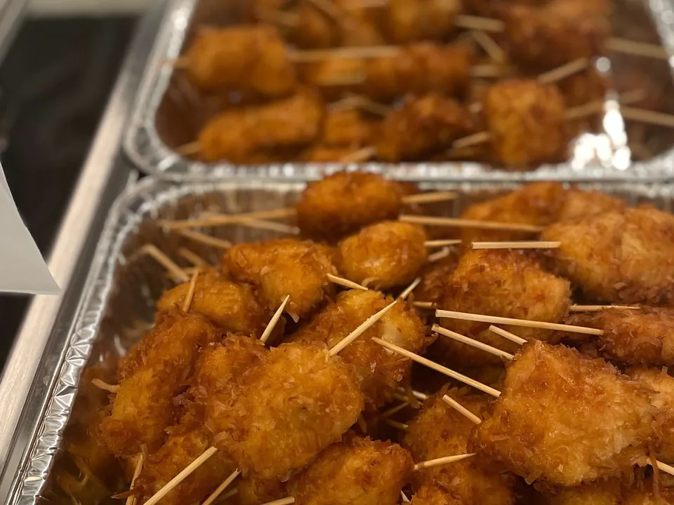 Foil catering pans of golden breaded fried chicken bites on serving picks on a buffet counter