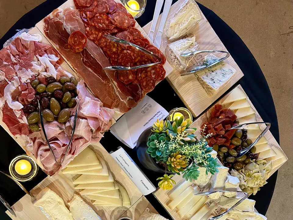 Overhead view of a build-your-own charcuterie station with separate boards of prosciutto, salami, and chorizo, soft and aged cheeses, and olives, each with its own serving tongs