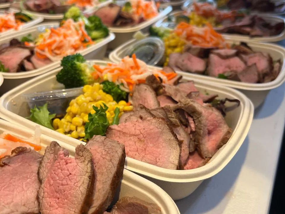 Individual boxed meals of sliced roast beef with broccoli, corn, and slaw for Dallas office catering