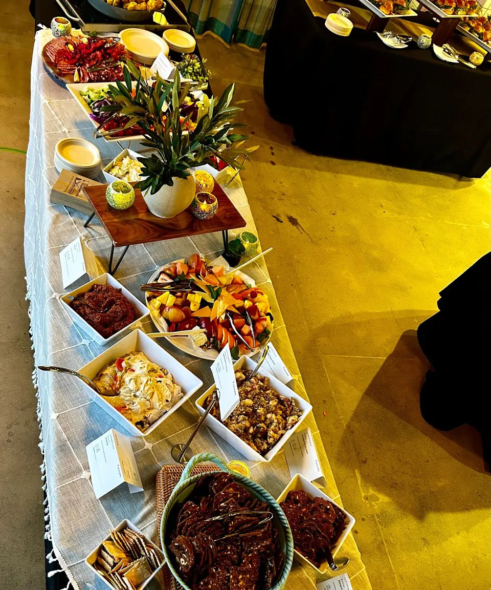 A grazing table shot down the line, with white serving boxes of mezze, marinated vegetables, dips, and crudite running the length of the table and a greenery riser raising the spread in the middle