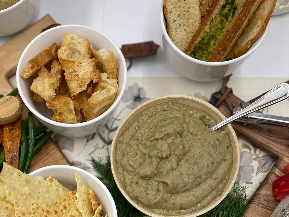 Overhead detail of a grazing table zone with a bowl of baba ganoush, crostini, pita crackers, crudite, and fresh herbs scattered between the bowls to fill the gaps