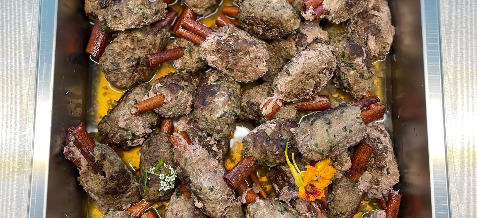 Hotel pan of grilled halal kofta kebabs garnished with herbs and edible flowers, the signature protein for halal office catering
