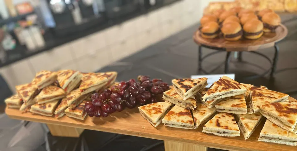 Mini paninis and sliders on wooden risers with red grapes at an office happy hour