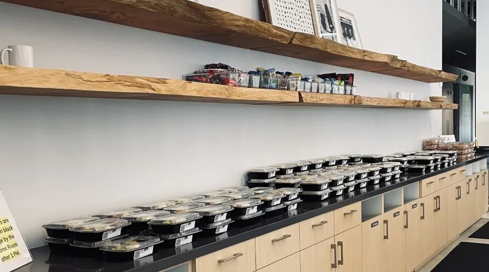 Rows of individually sealed boxed meals lined along a hospital break-room counter for clinical staff to grab between patients across shifts