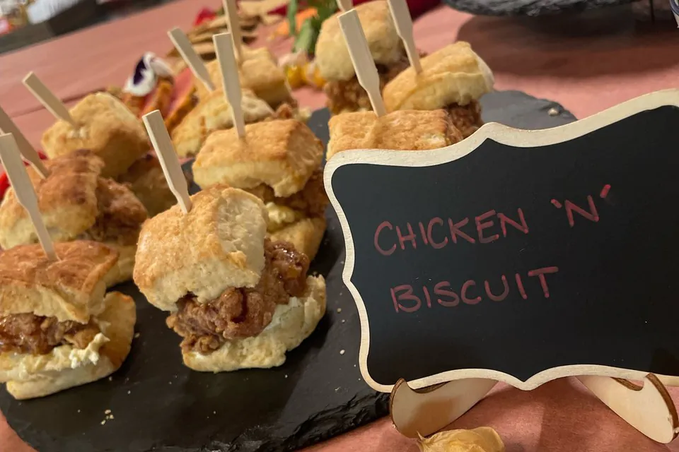Mini chicken and biscuit sliders speared on bamboo picks, lined up on a black slate platter for passed service