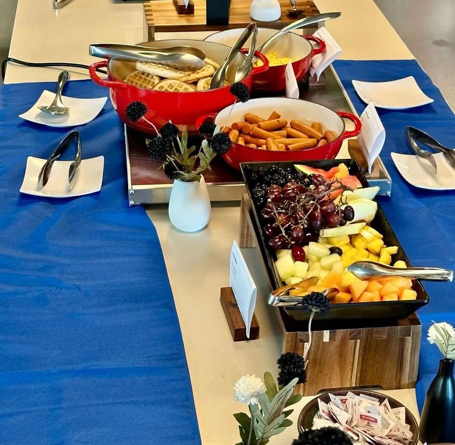 Breakfast buffet line with a red Dutch oven of waffles, a tray of French toast sticks and fresh fruit on an office table