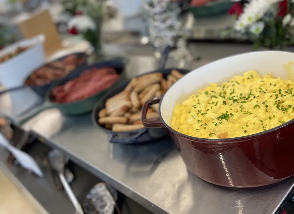IHOP style breakfast combo proteins: a pot of scrambled eggs beside bowls of bacon and sausage links on an office catering counter
