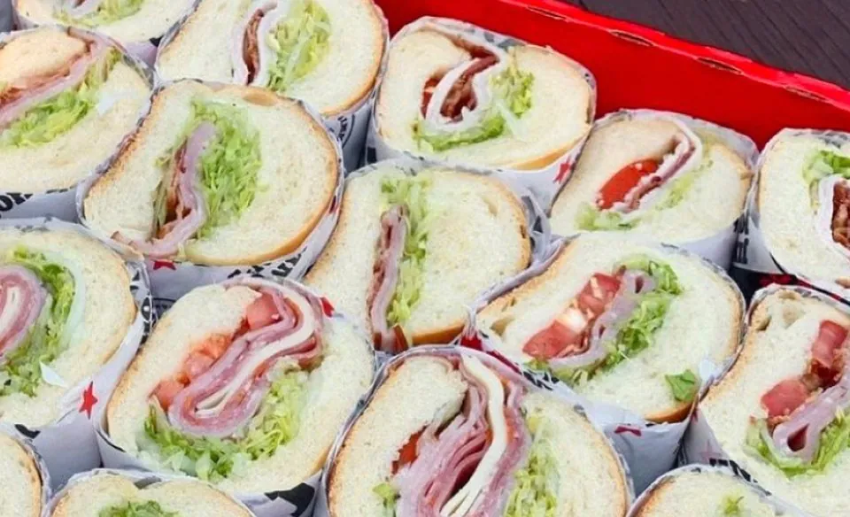 Overhead view of a Jimmy John's catering party box of eight-inch subs sliced in half with ham, turkey, bacon, lettuce and tomato