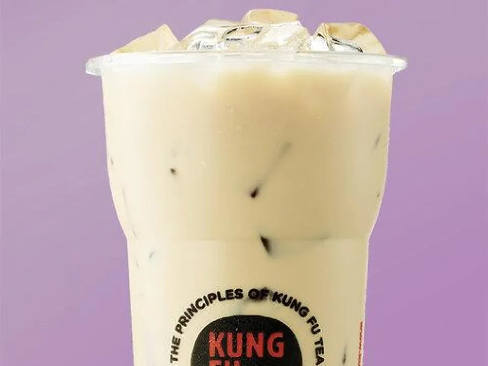 A tall clear cup of creamy iced Kung Fu Tea milk tea over ice on a soft purple background