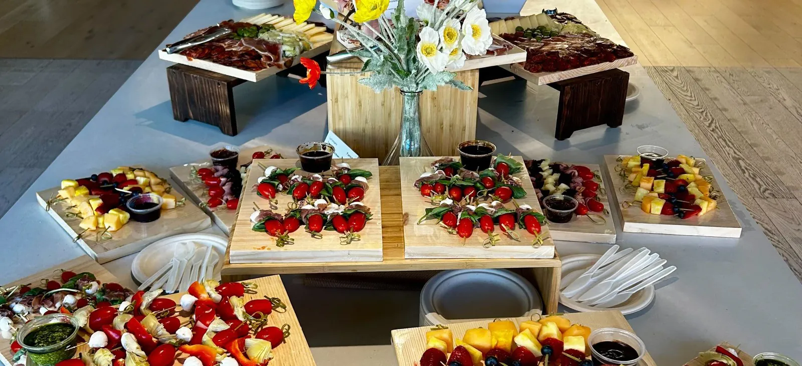 Upscale law firm office catering spread with caprese skewers, charcuterie, and fresh fruit arranged on butcher-block risers along a long conference-floor table
