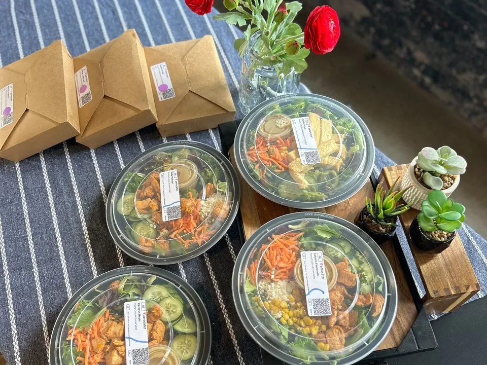 Overhead view of individual round salad bowls with grilled chicken, corn, and vegetables alongside kraft takeout boxes, the grab-it-at-your-seat portion for a lunch and learn
