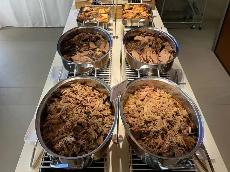 Office barbecue buffet with oval chafing dishes of pulled pork, sliced brisket, and roasted chicken plus rolls and sides