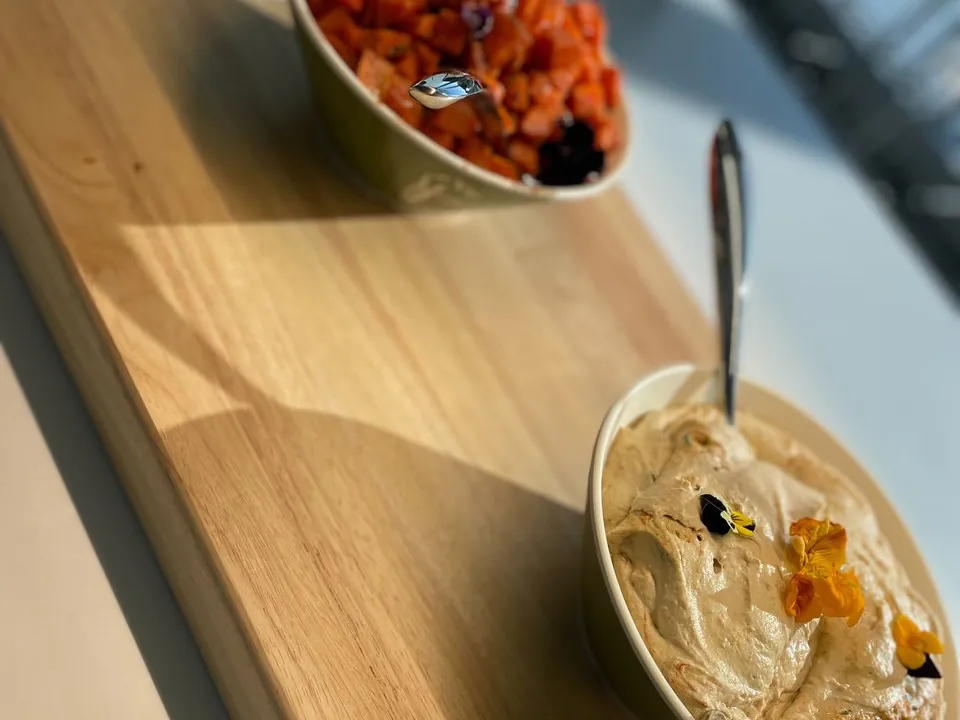 Mediterranean mezze on a wooden board with a bowl of hummus topped with edible flowers and a roasted sweet-potato and tomato salad