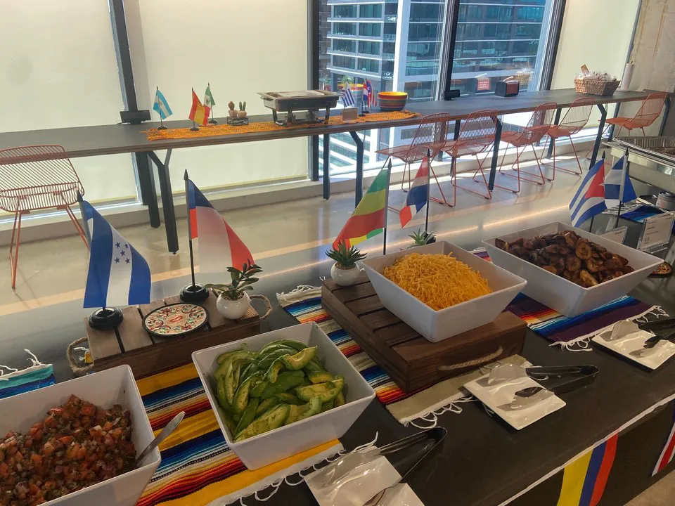 Build-your-own taco bar with white bowls of pico de gallo, sliced peppers, shredded cheese, and grilled vegetables on a striped runner