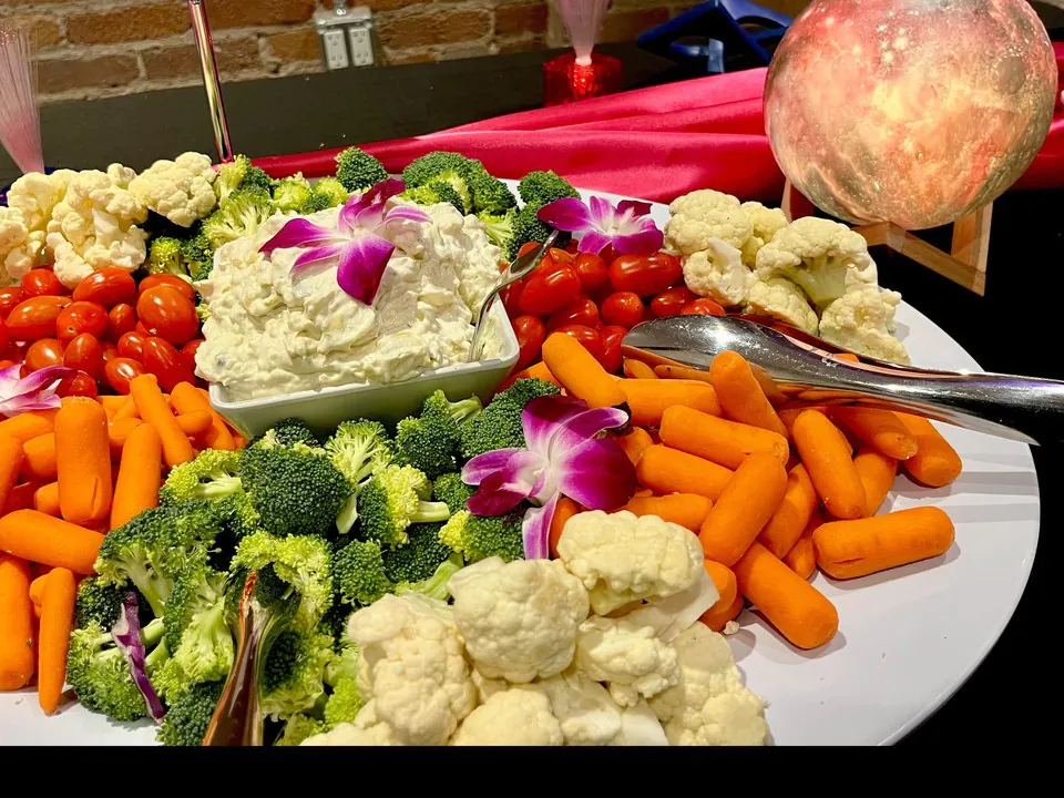 Round veggie crudite party tray with baby carrots, broccoli, cauliflower, and cherry tomatoes arranged around a center bowl of creamy dip