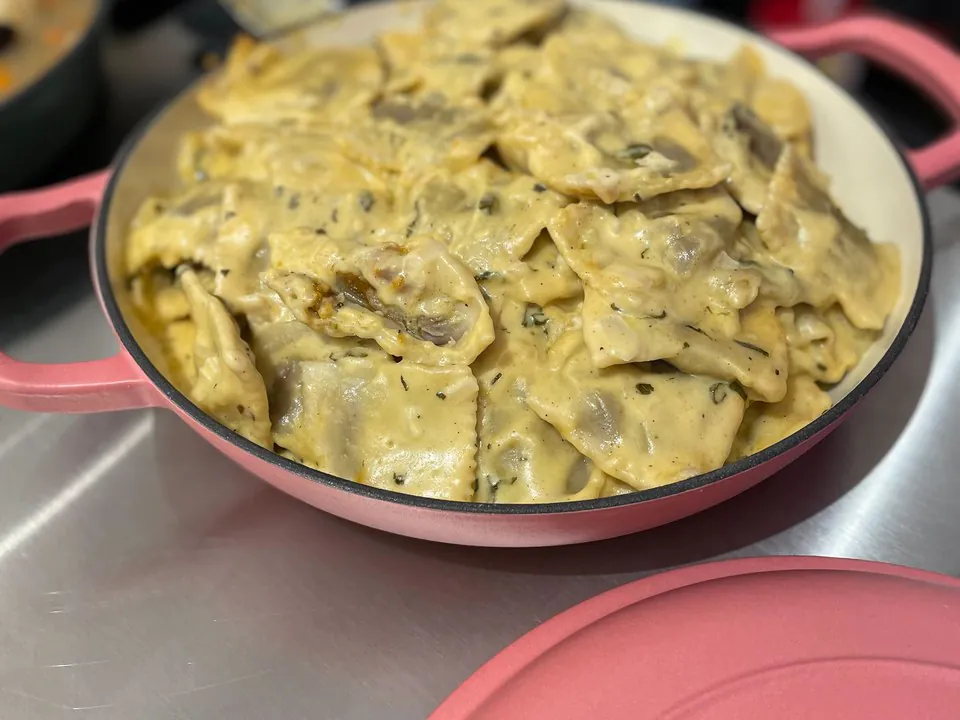 A pan of creamy mushroom ravioli in a pink enameled dish, one of the hot pasta options on a build-your-own pasta bar
