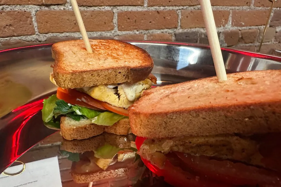 A finished build from the sandwich bar: a club sandwich cut in half on toasted bread with lettuce, tomato, and chicken, held together with picks on a silver platter
